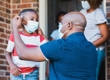 istockphoto-1254705429-170667a A mid adult father helps his young son put on a protective face mask before leaving their home amid the coronavirus pandemic.
