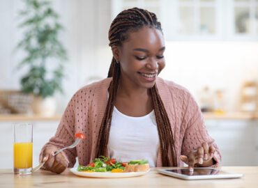 istockphoto-1301598077-170667a Smiling Young Black Woman Using Digital Tablet While Having Breakfast In Kitchen At Home, Positive African American Female Sitting At Table, Checking Social Networks Or Shopping Online, Copy Space